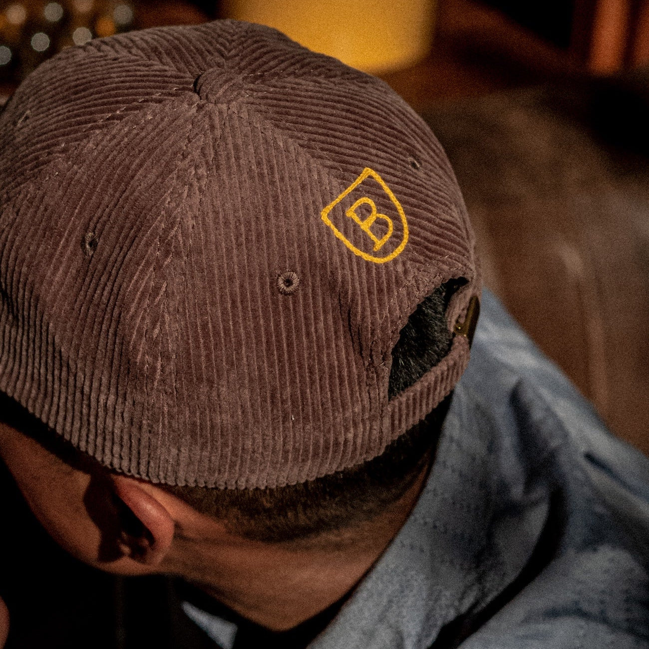 Back of a person wearing a brown cap with a 'B' logo, sitting indoors