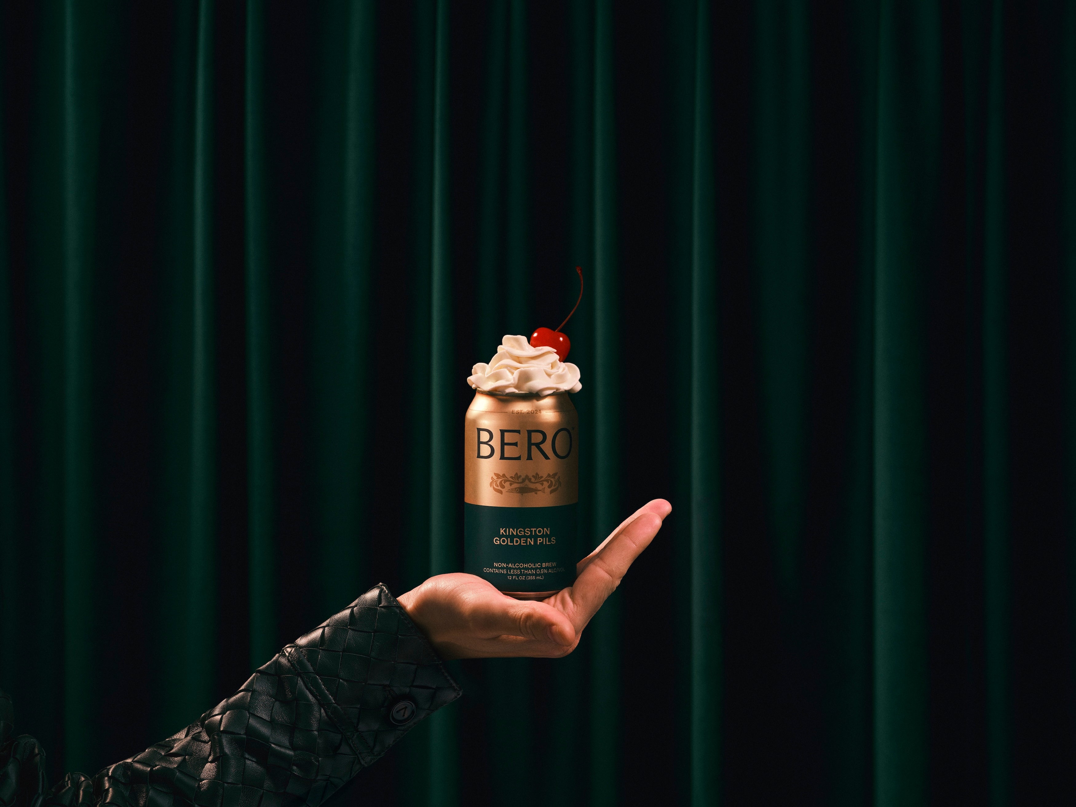Hand holding a can of Kingston Golden Pils with cream and a cherry on top
