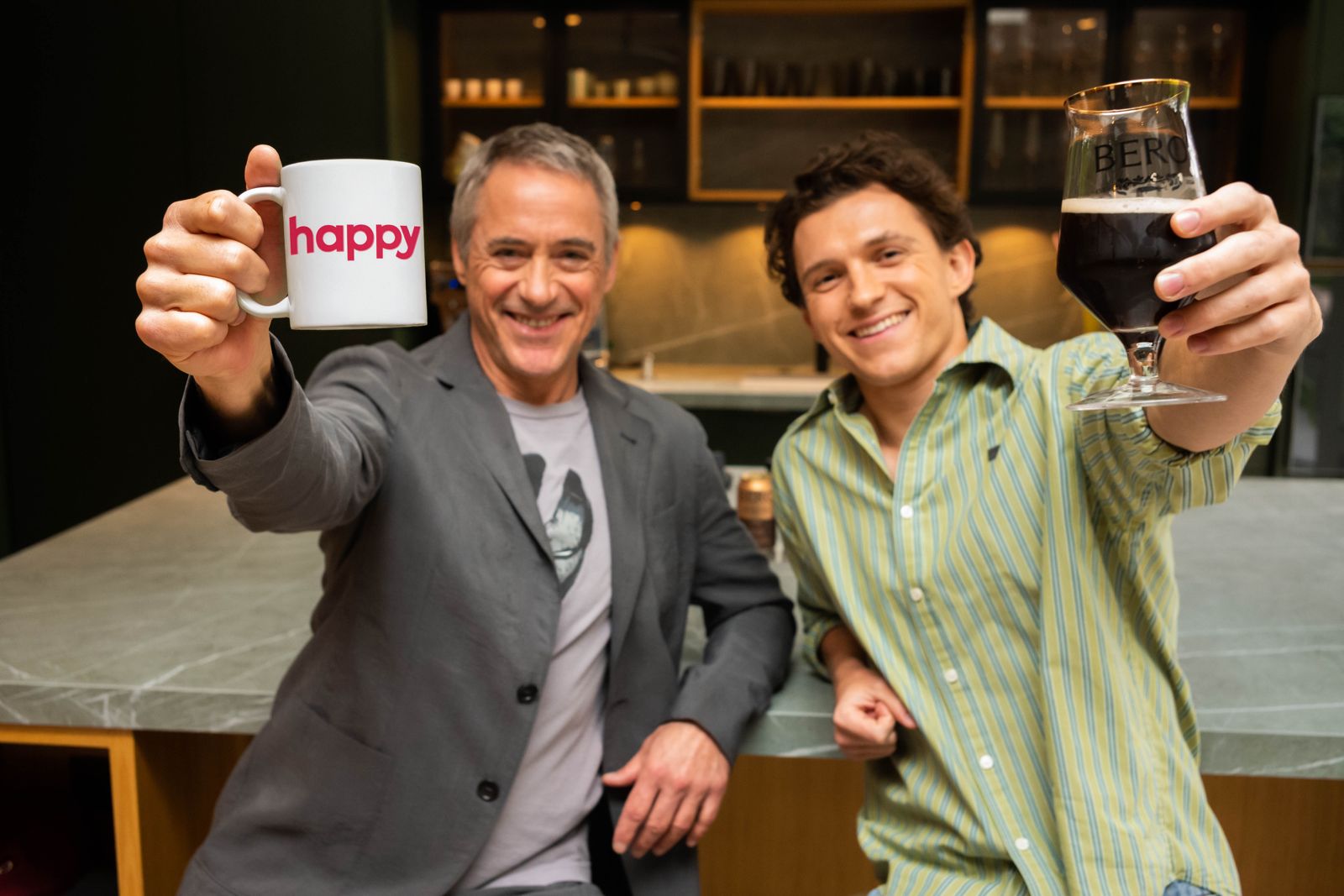Robert Downey, Jr and Tom Holland in a kitchen, one holding a mug with 'happy' and the other with a BERO beer glass