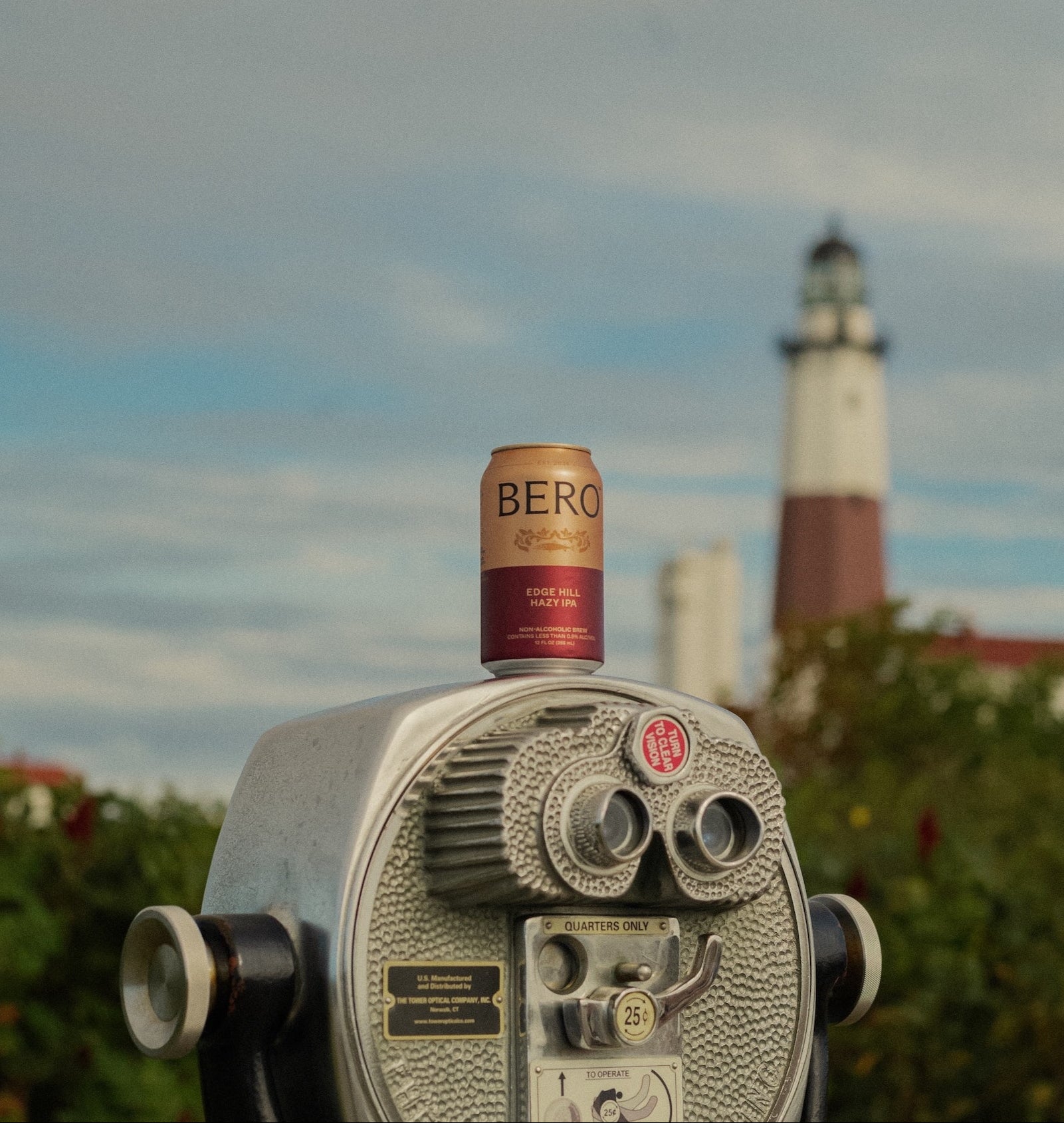 Can of beer on a binoculars with a lighthouse in the background
