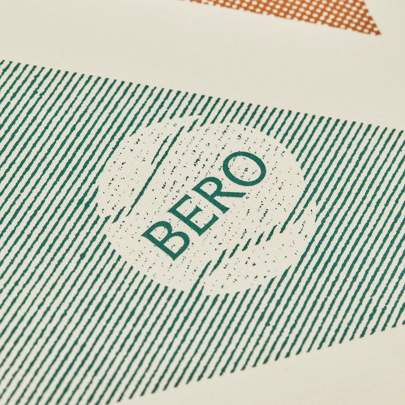 Close-up of green lined pattern on cream fabric with "BERO" text in circular design