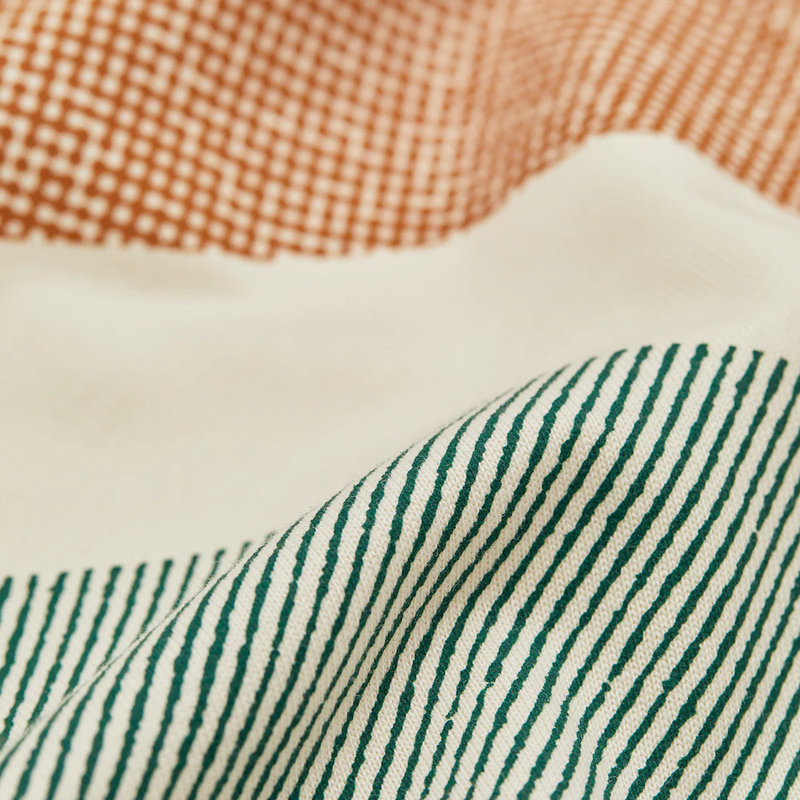 Close-up of cream-colored t-shirt fabric with orange dotted pattern and green striped design