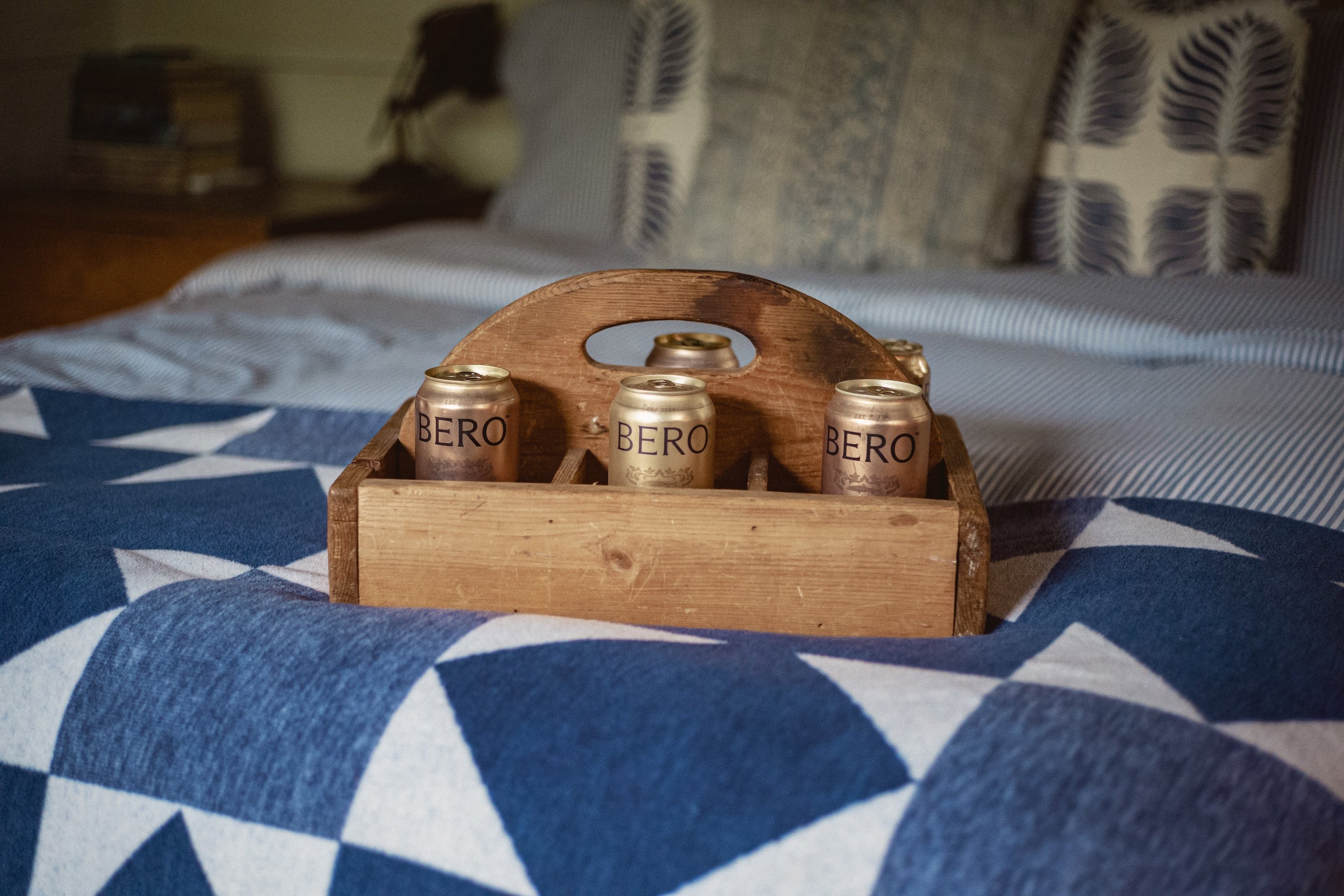 Wooden crate with BERO cans on a bed with a blue and white quilt