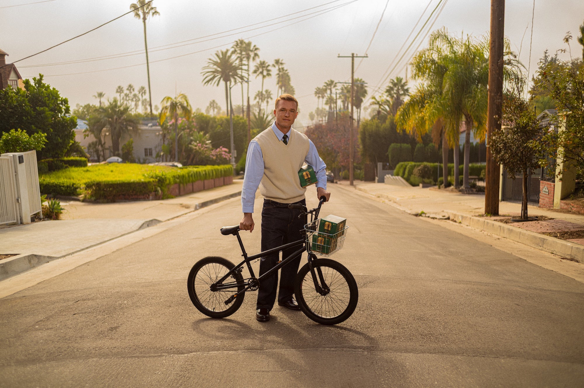 Man holding a bicycle wand cartons of BERO on a suburban street with palm trees in the background