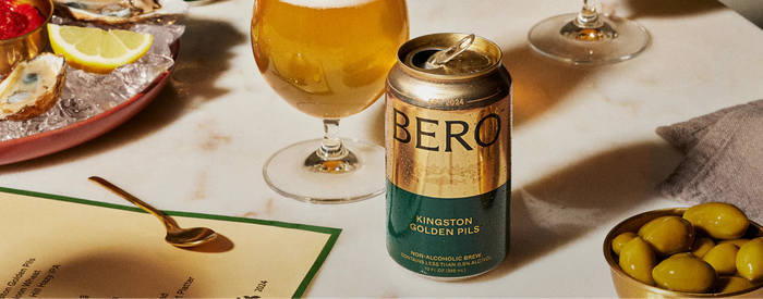 Can of BERO beer on a table with a glass of beer, oysters, and olives