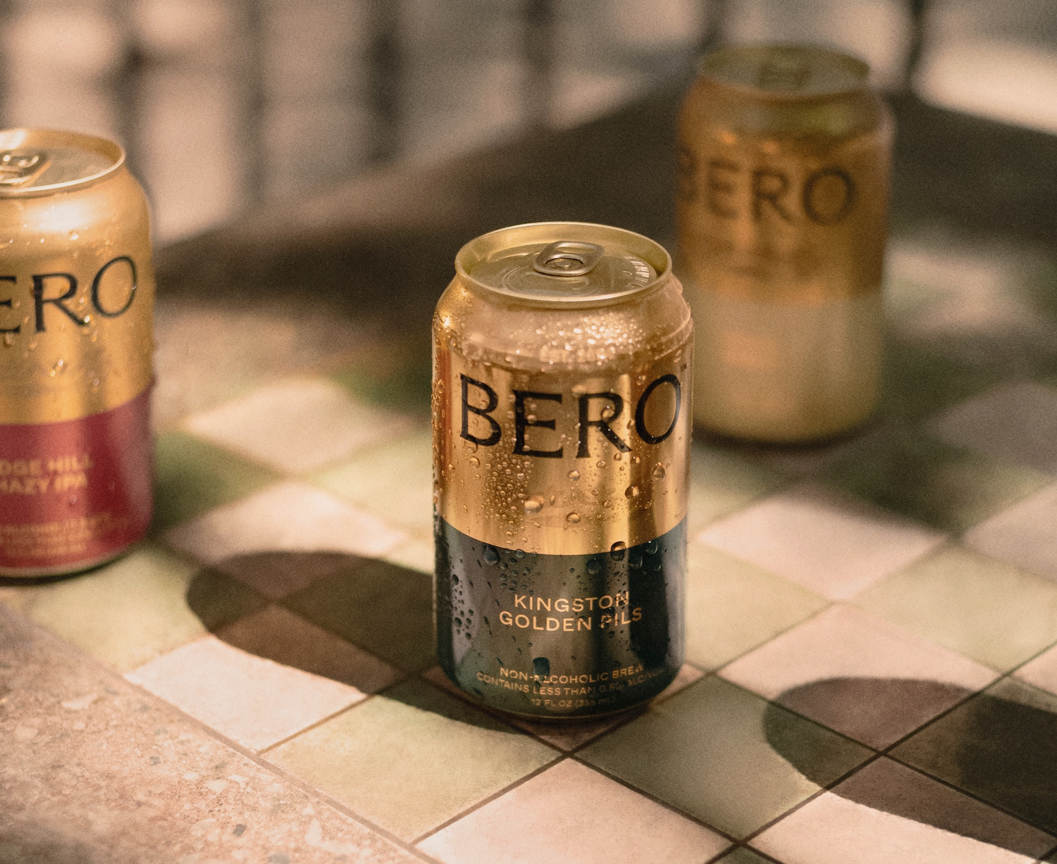 Three cans of Bero beer on a checkered tile surface