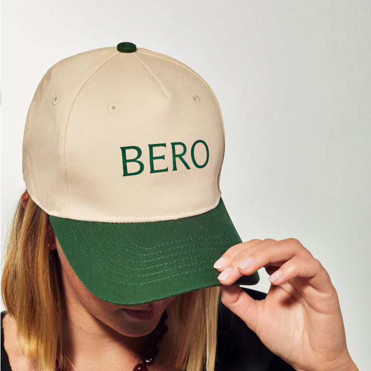 Person wearing cream and green BERO cap, adjusting the brim with their hand