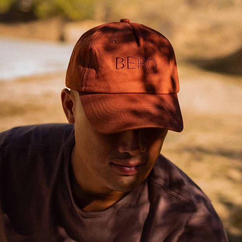 Person wearing a rust-colored tie-dye baseball cap with "BERO" embroidered text, looking downward