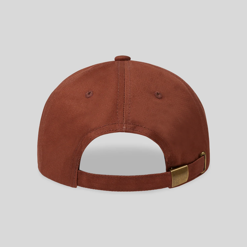 Back view of rust-colored baseball cap with adjustable brass buckle strap and ventilation eyelets