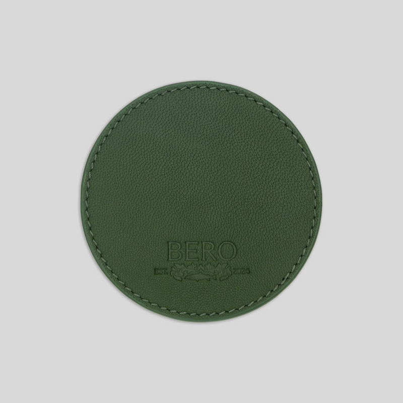 Round green leather coaster with embossed BERO logo and decorative stitching around the edge