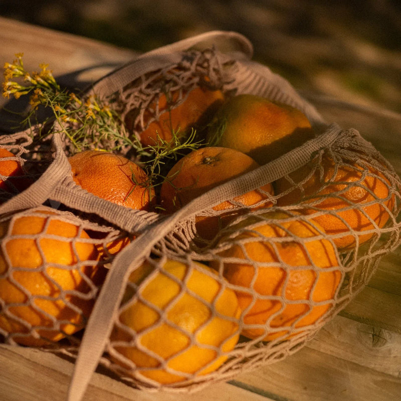 Fresh oranges in woven mesh bags with herbs, suggesting citrus ingredients for craft brewing