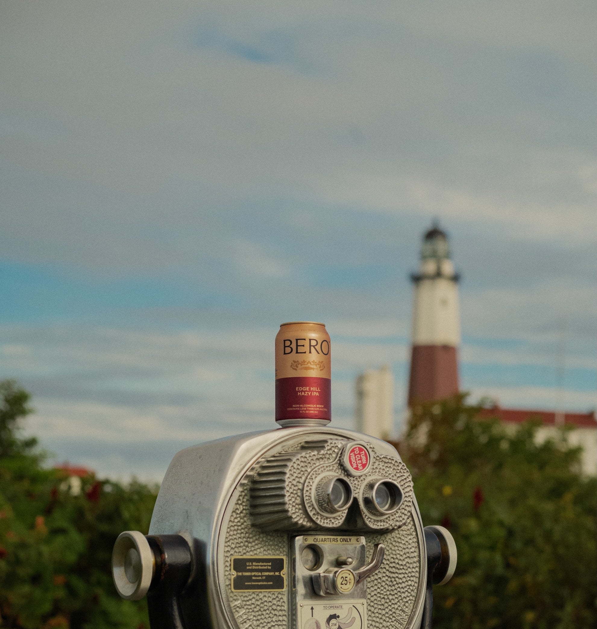 Can of beer on a binoculars with a lighthouse in the background