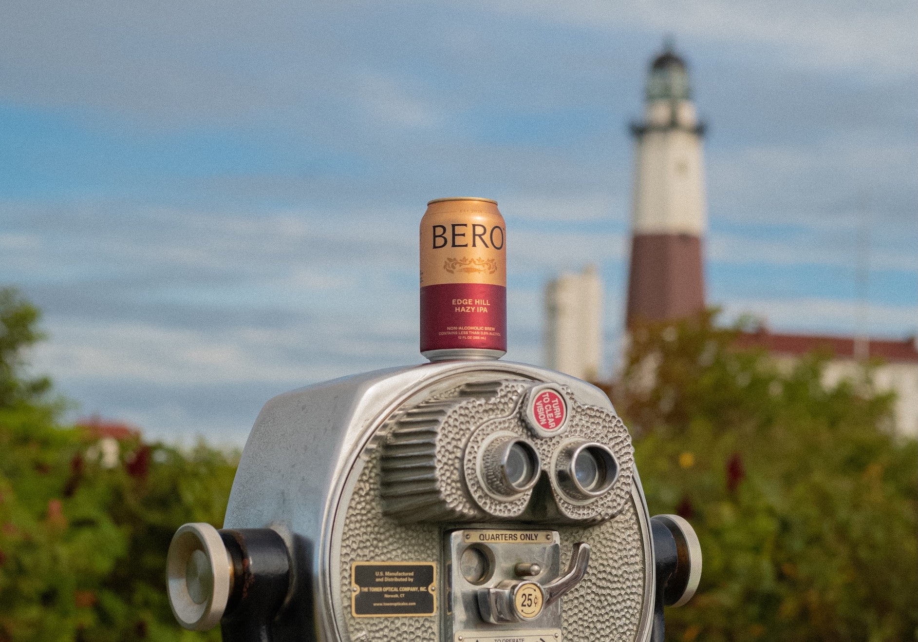 Coin-operated binocular with a can of BERO on top, with a lighthouse in the background