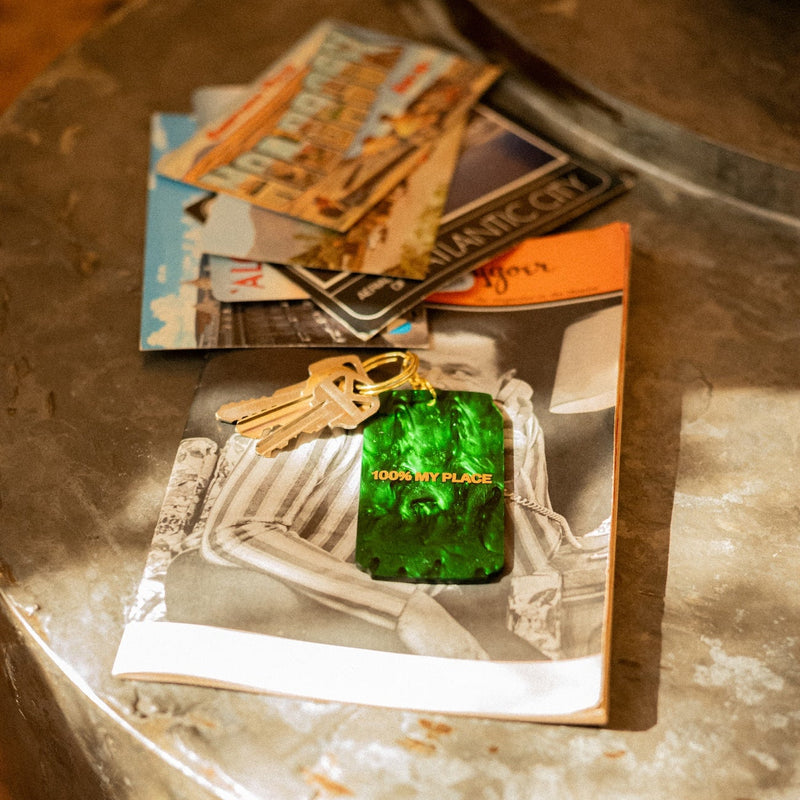 Green translucent keychain with "100% MY PLACE" text on keys, displayed on polaroid photos