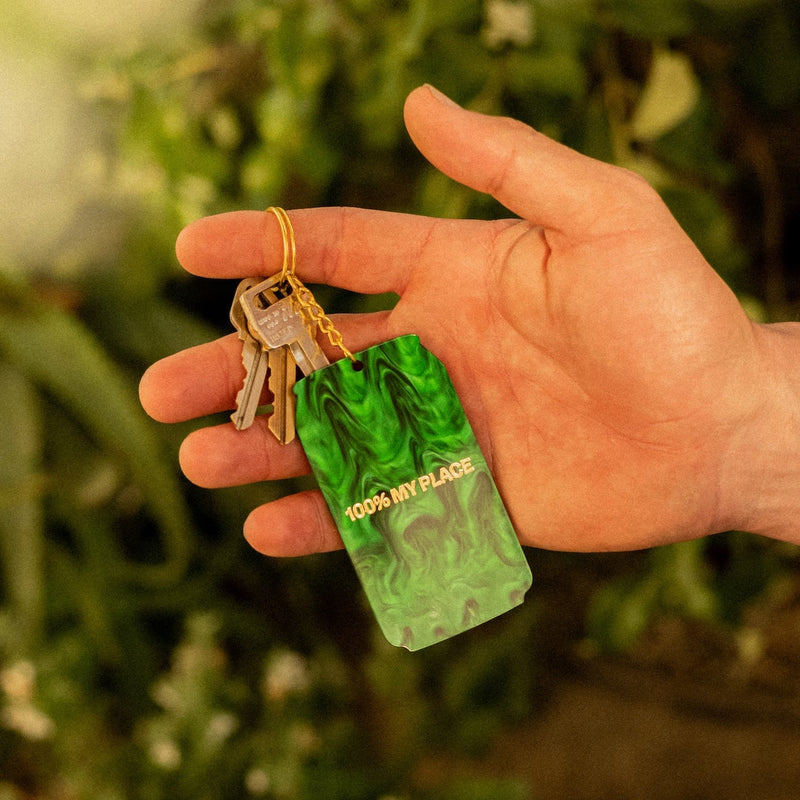 Hand holding green marbled keychain with "100% MY PLACE" text and attached keys