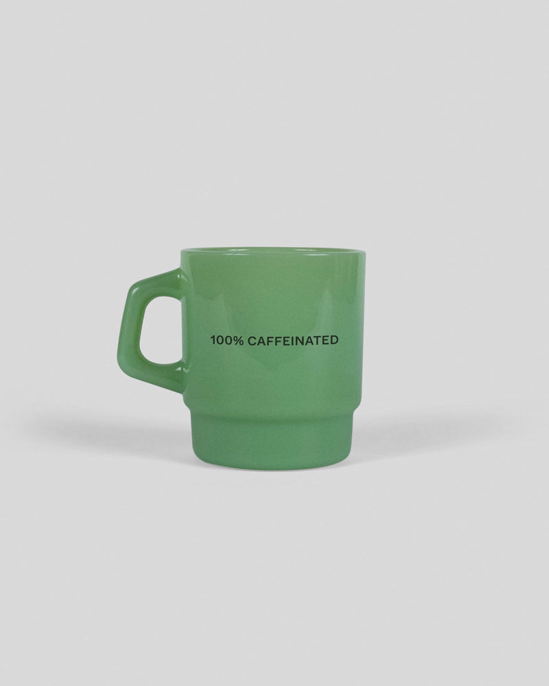 Green ceramic mug with "100% CAFFEINATED" text printed in black letters on the side