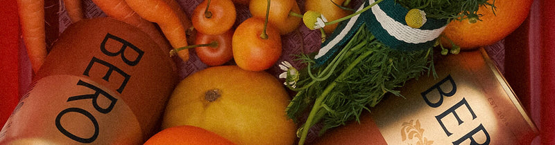 Fresh produce including oranges, greens, and herbs arranged in woven baskets with "BERO" branded paper bags