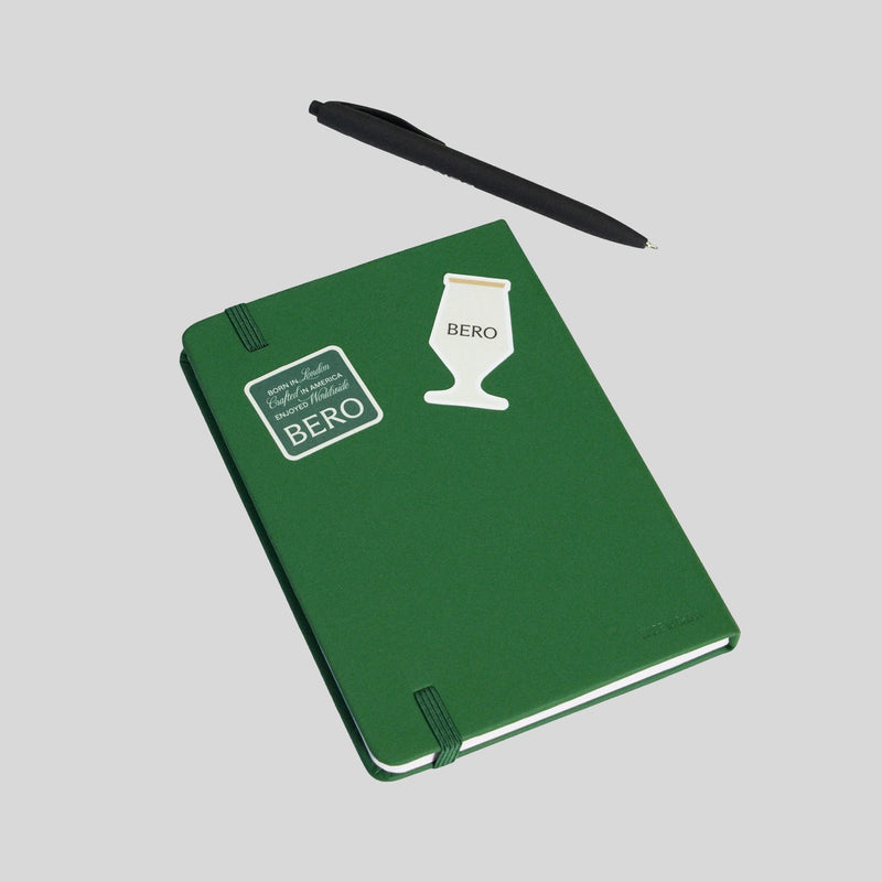 Green notebook with BERO logo and beer glass icon, accompanied by a black pen on white background