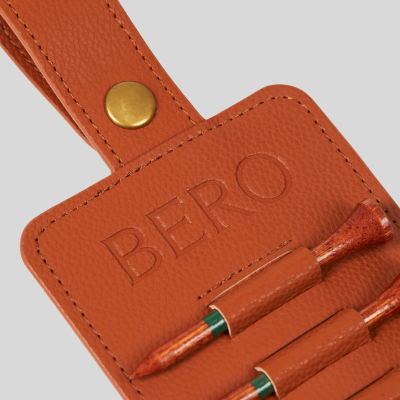 Orange leather golf tee holder with "BERO" embossed text, brass snap closure, and wooden golf tees secured in loops