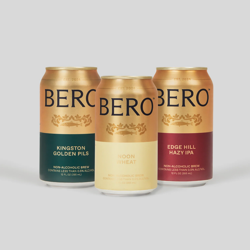 Three BERO non-alcoholic beer cans in gold packaging: Kingston Golden Pils, Noon Wheat, and Edge Hill Hazy IPA